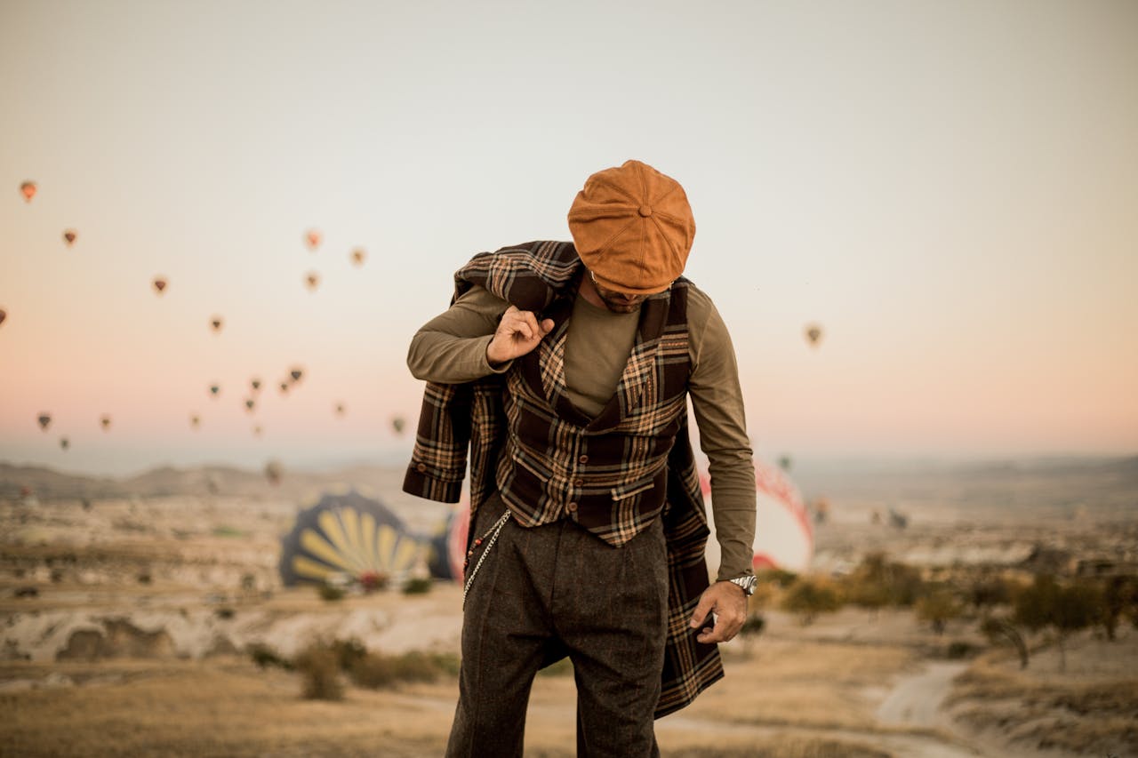 Stylish man in vintage attire amidst a stunning Cappadocia sunrise with hot air balloons.