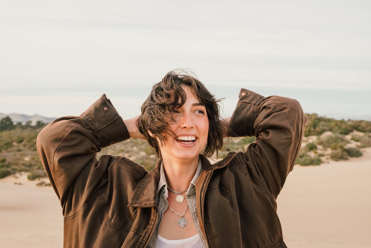 portfolio-img-02 Smiling woman wearing a brown coat enjoying a windy beach day.