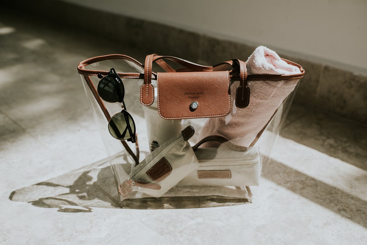 portfolio-img-09 A clear handbag with leather accents, sunglasses, and a towel, capturing a sunny day indoors.
